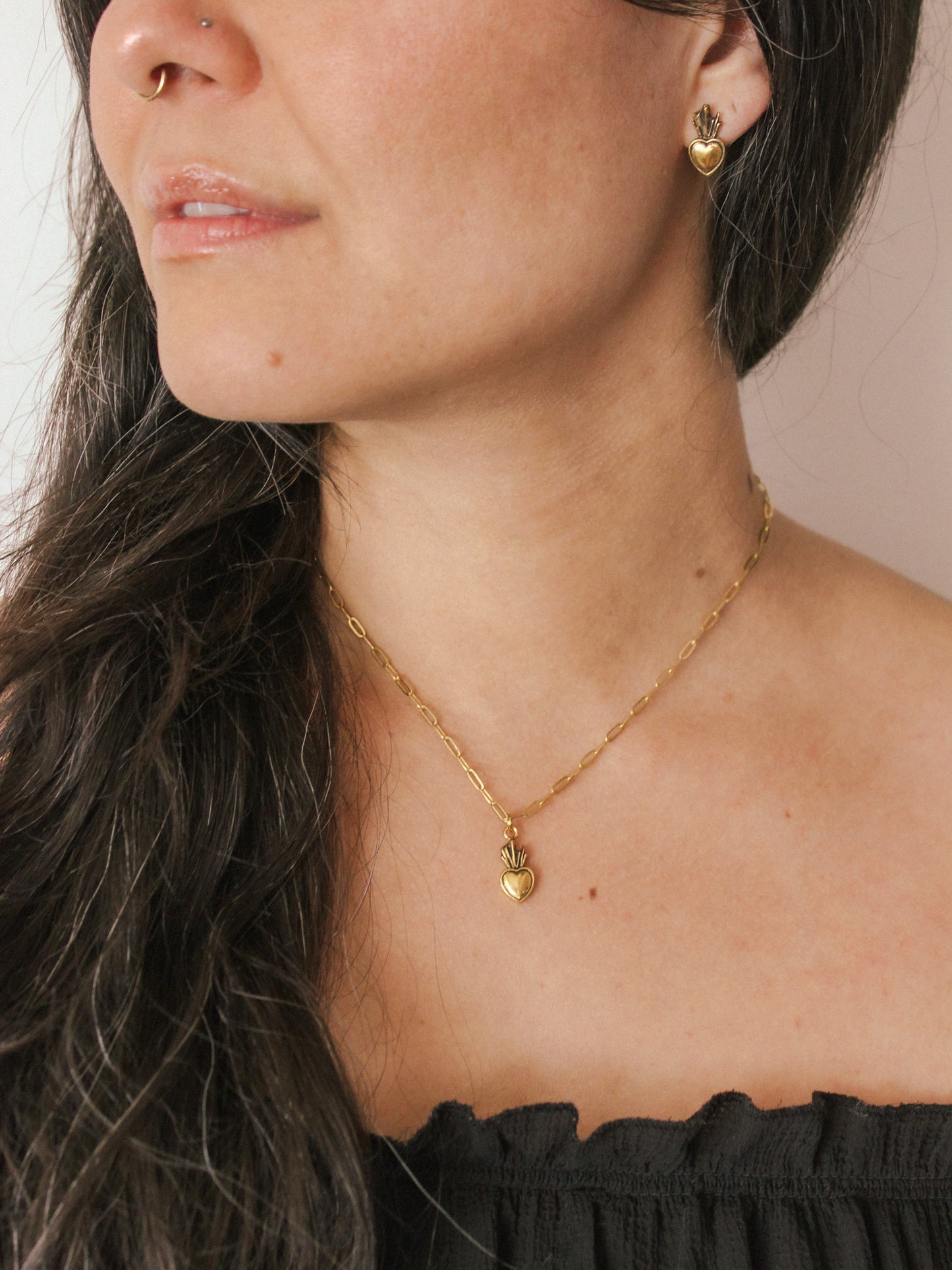 Close-up of a person wearing a gold necklace with heart pendant and gold heart earrings.