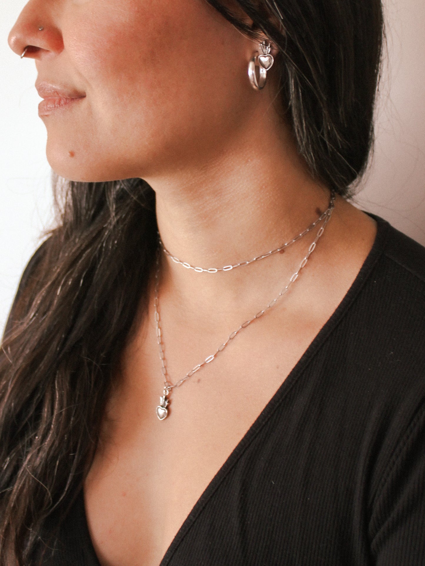 Close-up of a person wearing layered necklaces and earrings against a neutral background