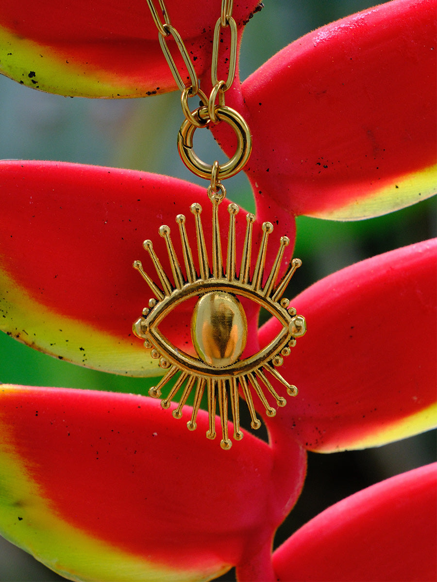 Yoté Jewelry Ojo Pendant in gold in front of Heliconia plant.