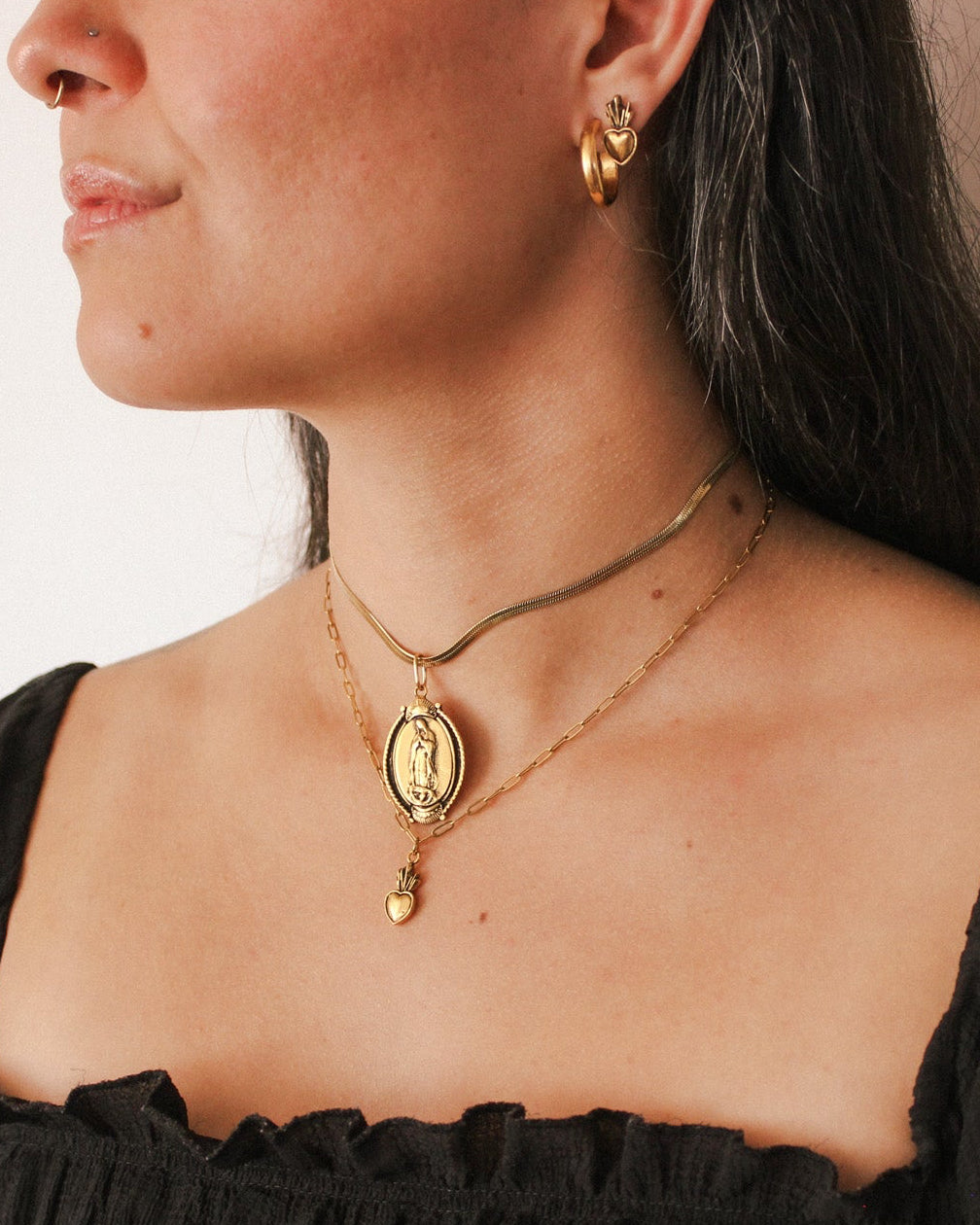 Woman wearing gold necklaces and earrings against a neutral background