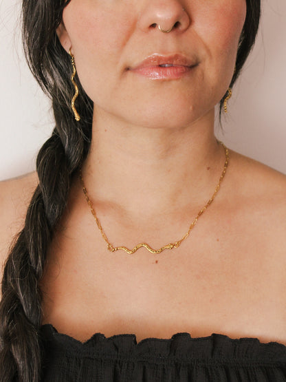 Woman wearing a gold necklace and earrings with a plain background