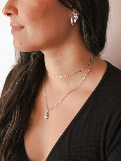 Close-up of a person wearing layered necklaces and earrings against a neutral background