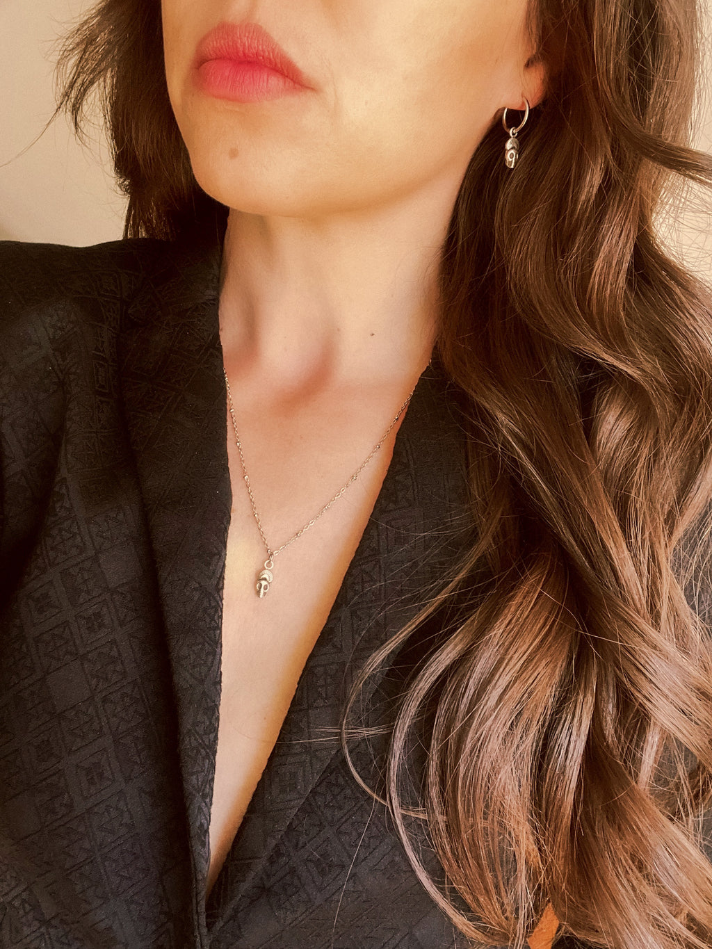 Close-up of a woman wearing a skull necklace and skull earrings with a neutral background