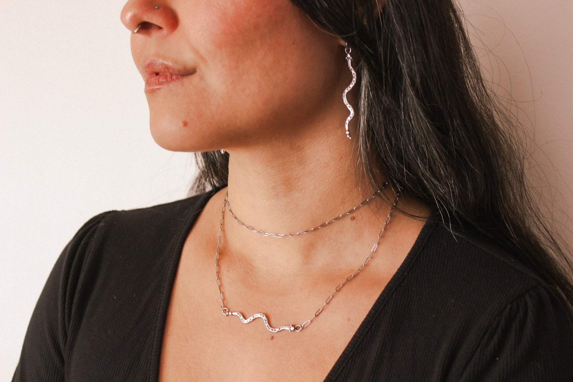 Woman wearing a silver snake necklace and snake earring against a neutral background