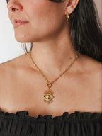 Gold necklace with an eye pendant worn by a person against a neutral background