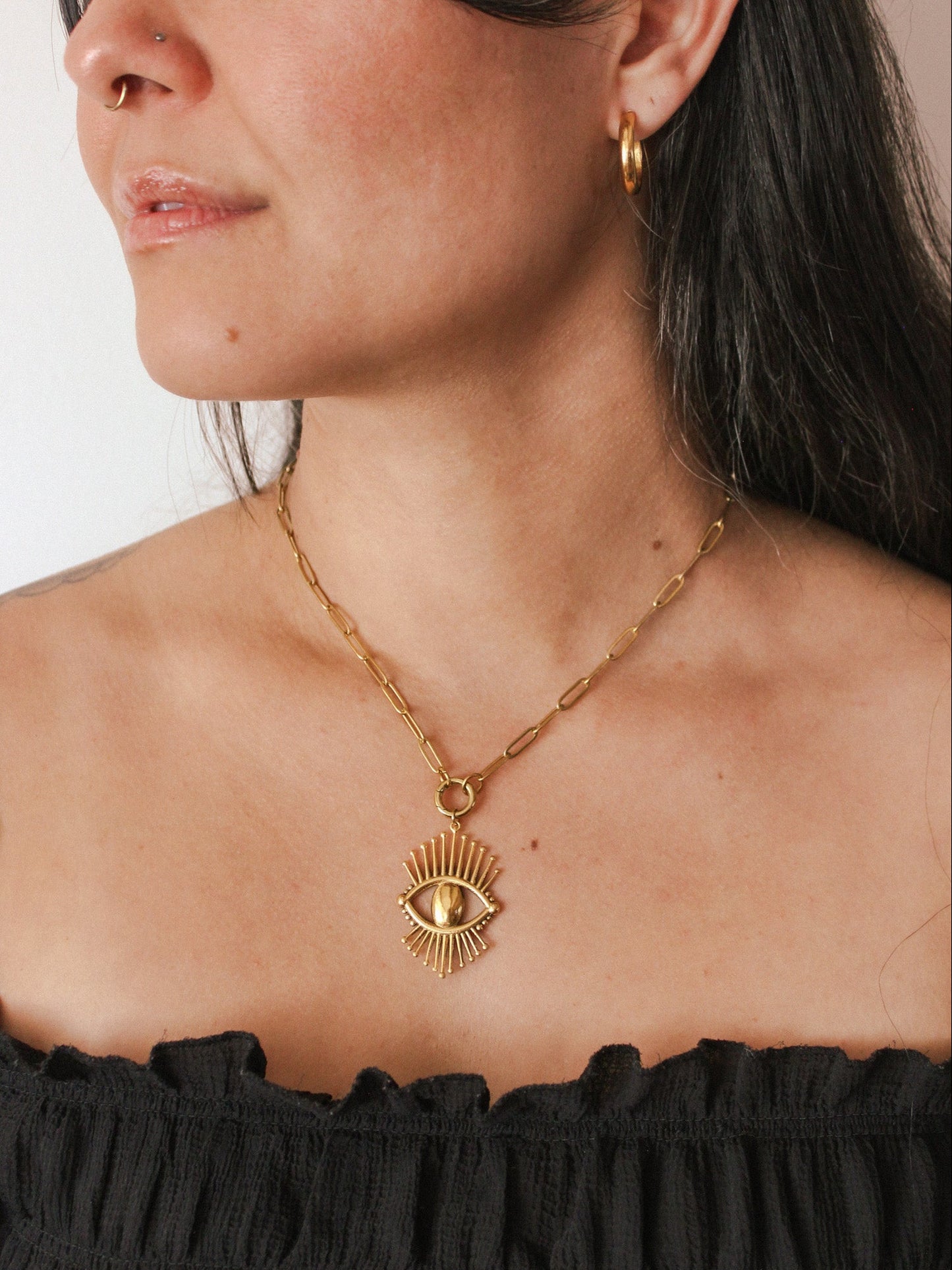 Gold necklace with an eye pendant worn by a person against a neutral background